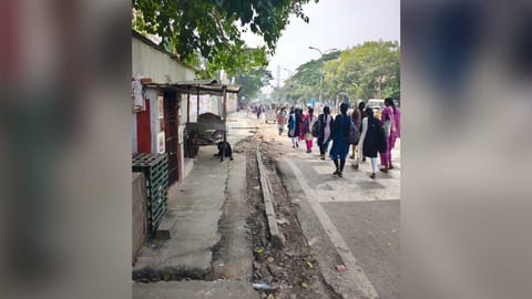 Pedestrians seen walking on Basin Bridge Road due to damaged pavement and encroachment.
