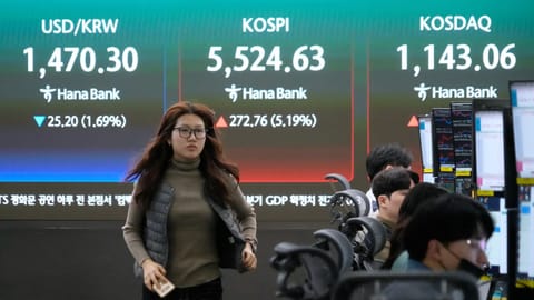 A currency trader passes by a screen showing the Korea Composite Stock Price Index (KOSPI), rear center, and the foreign exchange rate between U.S. dollar and South Korean won, rear left, at the foreign exchange dealing room of the Hana Bank headquarters in Seoul, South Korea.