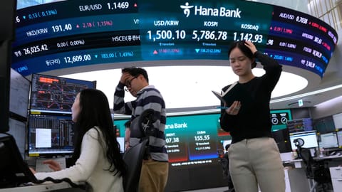 Currency traders work near a screen showing the Korea Composite Stock Price Index (KOSPI), top center, and the foreign exchange rate between U.S. dollar and South Korean won, top center left, at the foreign exchange dealing room of the Hana Bank headquarters in Seoul, South Korea, Thursday, March 19, 2026