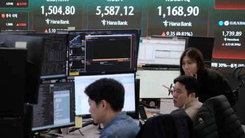Currency traders watch monitors near a screen showing the Korea Composite Stock Price Index (KOSPI), top center, and the foreign exchange rate between U.S. dollar and South Korean won, top left, at the foreign exchange dealing room of the Hana Bank headquarters in Seoul, South Korea, Thursday, March 26, 2026.