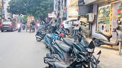 Two-wheelers and autorickshaws are parked on both sides of the road and pavements in Choolai