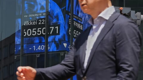 A person walks in front of an electronic board at a business building showing Japan's Nikkei index