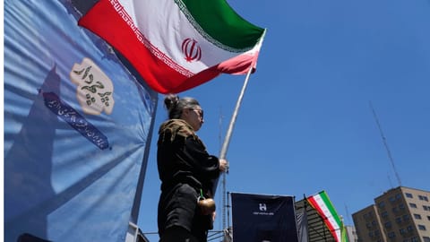 A woman waves an Iranian flag during a pro-government campaign as a portrait of the slain Supreme Leader Ayatollah Ali Khamenei, who was killed in U.S. and Israeli strikes