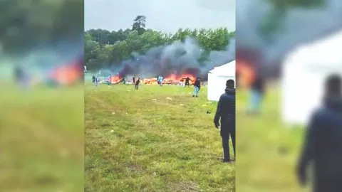 Flames engulfing the sky at an open-air festival with large white tents