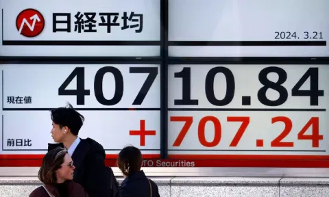 Passersby walk in front of an electric screen displaying Japan's Nikkei share average outside a brokerage in Tokyo