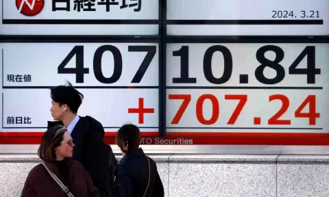 Passersby walk in front of an electric screen displaying Japan's Nikkei share average outside a brokerage in Tokyo (Reuters)