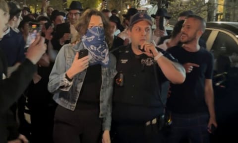 This image taken from video shows a woman and a police officer as they are pursued by a mob of Orthodox Jewish men in the Crown Heights section of Brooklyn (AP)