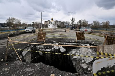 Cars ride past huge holes on a damaged bridge in Makariv, Kyiv region during the Russian invasion of Ukraine.