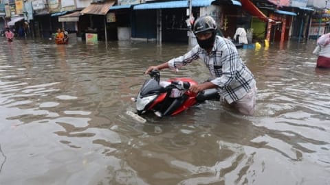 A biker moving his bike through an inundated road.