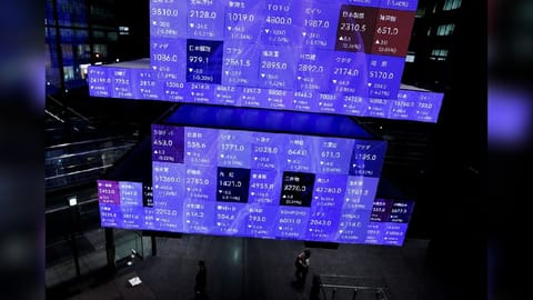 Visitors walk past Japan's Nikkei stock prices quotation board inside a conference hall in Tokyo