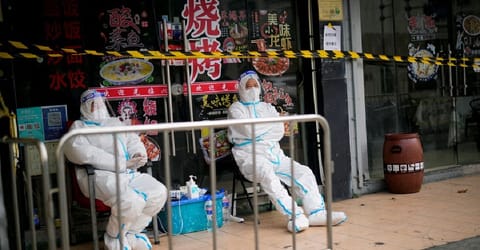 Workers in protective suits keep watch behind a barrier at a sealed restaurant area
