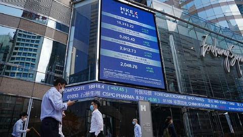 People walk past a screen displaying the Hang Seng stock index at Central district