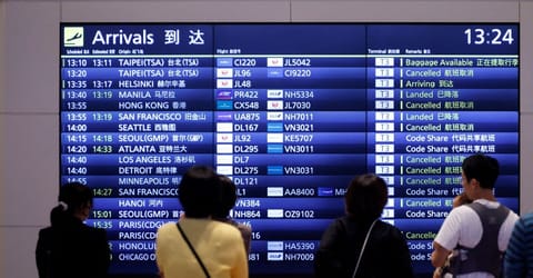 People stand in front of a flight information board at the Haneda International Airport