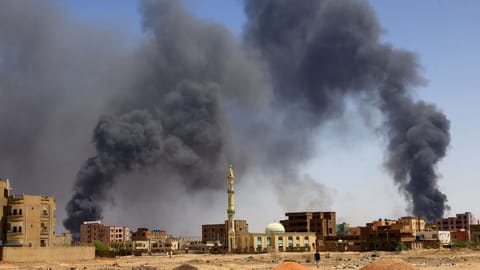 A man walks while smoke rises above buildings after aerial bombardment, during clashes between the paramilitary Rapid Support Forces and the army in Khartoum North