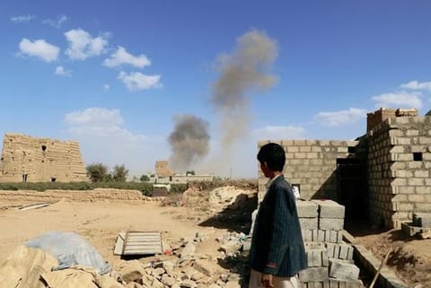 A boy looks at dust raising from the site of air strikes in Saada, Yemen