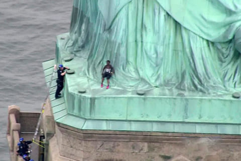A police officer climbs up a ladder to talk to a climber into descending the Statue of Liberty