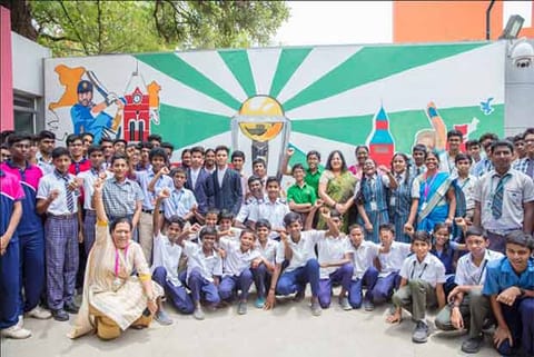 Students and their teachers pose in front of their artwork