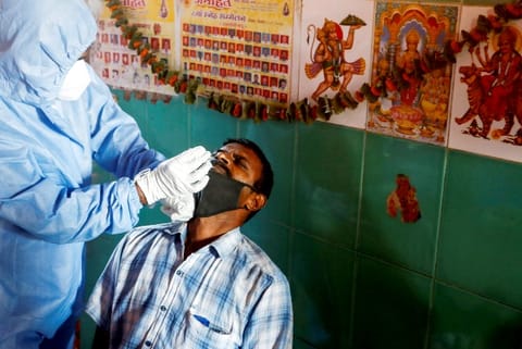 A health worker in personal protective equipment (PPE) collects a swab sample from a man