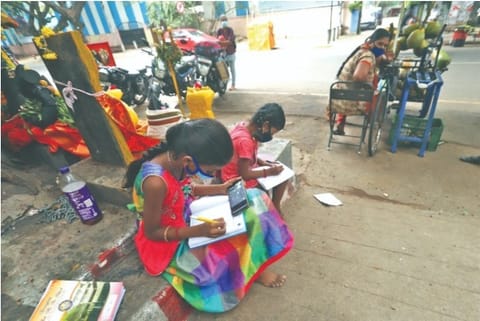 Two girls attending online class on the roadside while their mother, a tender coconut vendor, keeps