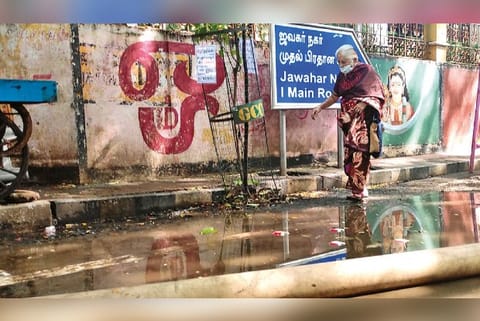 An elderly woman crossing a pool of rainwater at Jawahar Nagar