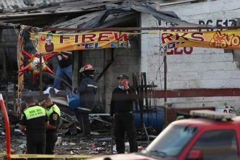 Firefighters and rescue personnel stand near a destroyed house