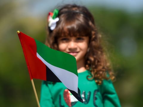 A child holding the UAE flag. The UAE flag was designed by a young Emirati, Abdullah Mohammad Al Maainah, after he came across an advertisement announcing a flag design competition.