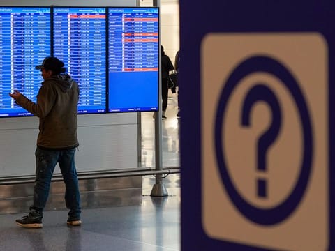 A person talks on a mobile phone by a video board showing flight delays and cancellations. Picture used for illustrative purposes.