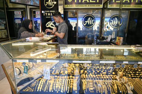 An employee helps a customer to buy gold jewellery at a market place on April 14, 2025.
