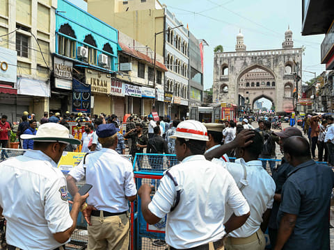 Fire personnel and police stand outside the Krishna Pearls building (blue-colored) that caught fire in Hyderabad on May 18, 2025.