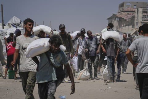 Palestinians carry sacks of flour unloaded from a humanitarian aid convoy that reached Gaza City from the northern Gaza Strip, Sunday, July 27, 2025.