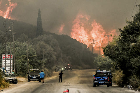 Inhabitants stand on a road as a wildfire burns a forest near the city of Patras, western Greece on August 12, 2025.