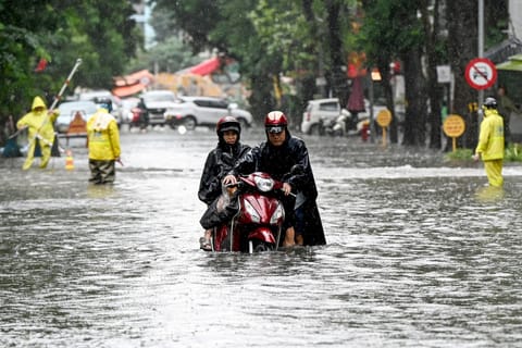 A man pushes his motorbike on a flooded street due to heavy rains caused by Tropical Storm Matmo in Hanoi on October 7, 2025.