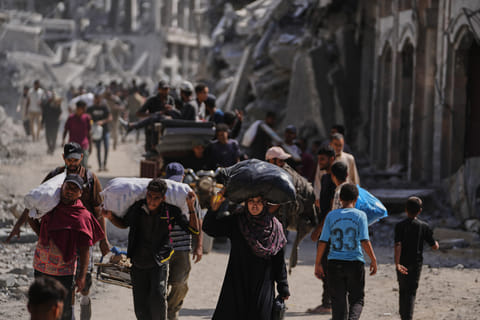 Displaced Palestinians walk with their belongings past destroyed buildings as they return to their homes in Khan Younis, southern Gaza Strip.