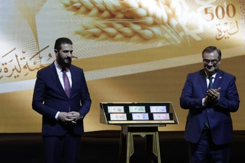 Syria's President Ahmed al-Sharaa (L) and Syria's Central bank chief Abdul Qadir al-Hasriya (R) stand between the country's new revamped currency notes at the Conference Palace in the Syrian capital Damascus on December 29, 2025.