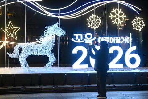 A woman takes a photo in front of a luminous sign for "2026" ahead of a countdown event for the New Year in Seoul on December 31, 2025.
