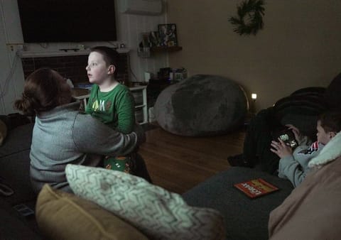 Ronan Murphy snuggles with his mom, Andrea, while looking at the snow falling outside his home while brother, Connor sits nearby in Ayer, Mass., on Saturday, Jan. 17, 2026. (AP Photo/Shelby Lum)