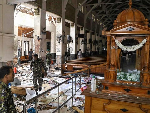 Sri Lankan security personnel walk past dead bodies covered with blankets amid blast debris at St. Anthony's Shrine following an explosion in the church in Kochchikade in Colombo on April 21, 2019.