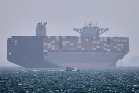 A container ship sits at anchor as a small motorboat passes in the foreground in the Strait of Hormuz off Bandar Abbas, Iran, on Saturday, May 2, 2026.