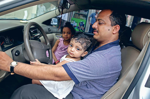 A young child sits on the lap of her father in a car. For illustrative purposes only.