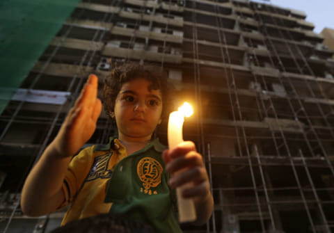 A Lebanese boy holds a candle in front of a damaged building. For illustrative purposes only.