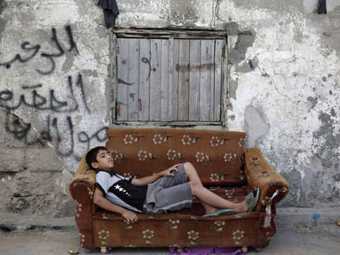 A boy rests on an old couch in front of a dilapidated house in Gaza where more than 40 per cent of people remain below the poverty line