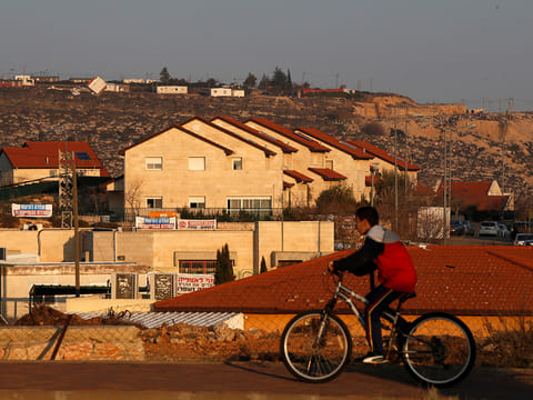 In this file picture, a boy rides his bicycle past houses in the Israeli colonies of Ofra, in the Occupied West Bank on February 6, 2017.