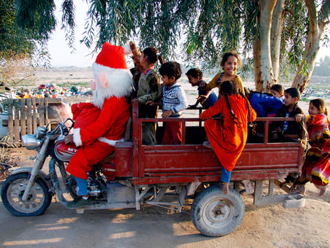 A man dressed in a Santa Claus outfit touring a popular neighbourhood on the outskirts of the Iraqi central city of Najaf, takes children on a ride in a tuktuk on December 25, 2018.
