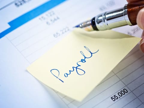A fountain pen checks a financial or business document with an adhesive note reading "payroll" attached to it.