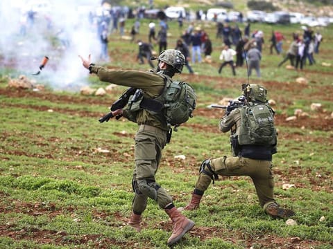 An Israeli soldier throws a tear gas canister at Palestinian demonstrators during a protest against Jewish settlements, in al-Mughayyir village near Ramallah