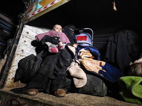 A woman wearing a niqab (full face veil) sits in the back of a truck carrying an infant and sitting next to pieces of luggage and a baby stroller, eastern Syrian Deir Ezzor province upon arriving with other fleeing families from remaining pockets held by Daesh.