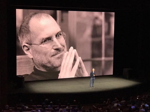 File photo shows CEO Tim Cook with an image of founder Steve Jobs in the background.