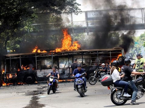 People drive their motorcycles near a burnt bus during anti-government protests, in Caracas, Venezuela April 30, 2019.