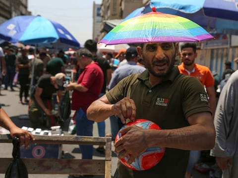 An Iraqi street vendor wears an umbrella-shaped hat to protect his head from the sun during a heat wave in the capital Baghdad