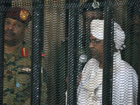 Sudan's deposed military ruler Omar al-Bashir stands in a defendant's cage during the opening of his corruption trial in Khartoum on August 19, 2019.